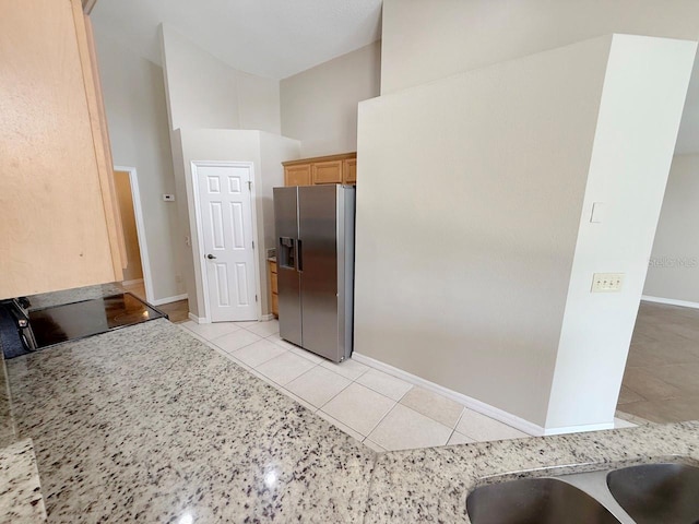 kitchen with stainless steel refrigerator with ice dispenser, light tile patterned floors, a towering ceiling, light countertops, and range