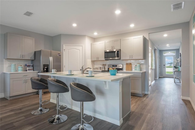 1902 Walnut Creek Dr, Kissimmee, FL 34744 - kitchen featuring stainless steel appliances, decorative backsplash, dark wood-style flooring, a kitchen bar, and light countertops