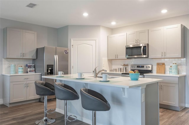 1902 Walnut Creek Dr, Kissimmee, FL 34744 - kitchen with stainless steel appliances, a breakfast bar, backsplash, wood finished floors, and light countertops