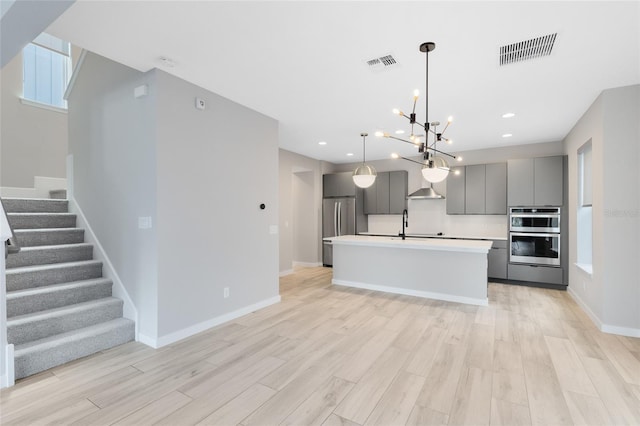 8290 Nemours Pkwy, Orlando, FL 32827 - kitchen featuring gray cabinetry, appliances with stainless steel finishes, light wood-style floors, a chandelier, and a kitchen island with sink