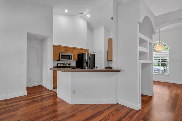 12713 Pine Arbor Dr, Clermont, FL 34711 - kitchen with appliances with stainless steel finishes, high vaulted ceiling, wood finished floors, brown cabinetry, and a chandelier