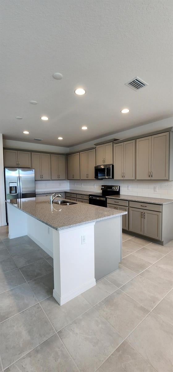 483 Shadow Gorge Way, Eustis, FL 32736 - kitchen featuring appliances with stainless steel finishes, a large island with sink, light stone countertops, light tile patterned floors, and recessed lighting