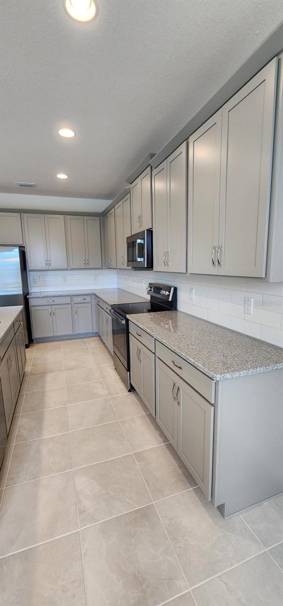 483 Shadow Gorge Way, Eustis, FL 32736 - kitchen featuring stainless steel appliances, gray cabinetry, light tile patterned floors, light stone counters, and recessed lighting