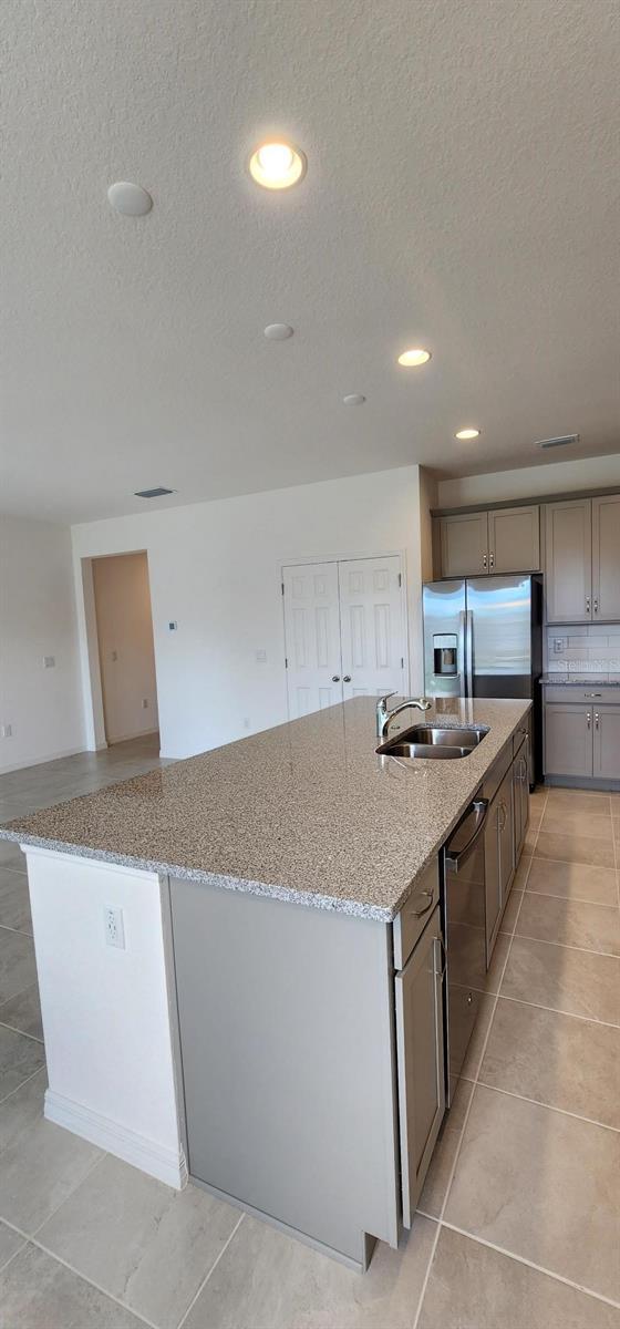 483 Shadow Gorge Way, Eustis, FL 32736 - kitchen featuring stainless steel appliances, a large island, a textured ceiling, light stone countertops, and light tile patterned floors