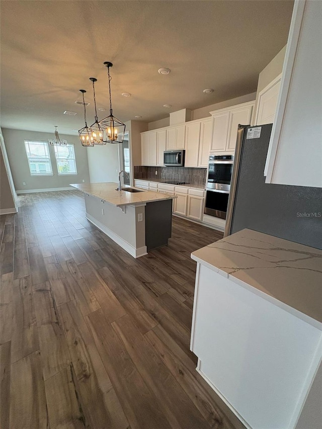 2318 Raven Ridge Rd, Minneola, FL 34715 - kitchen featuring stainless steel appliances, dark wood-style floors, decorative backsplash, white cabinetry, and a kitchen island with sink
