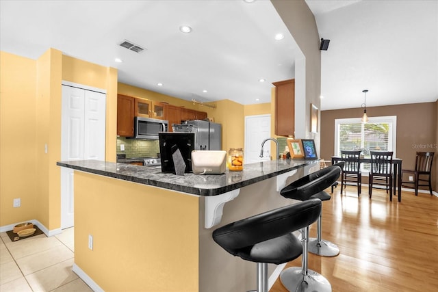 9275 Lake Sharp Ct, Orlando, FL 32817 - kitchen featuring stainless steel appliances, a peninsula, a kitchen breakfast bar, brown cabinets, and backsplash