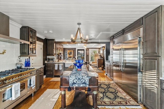 8407 Interbay Blvd, Tampa, FL 33616 - kitchen with premium appliances, wall chimney exhaust hood, light wood-style flooring, dark brown cabinets, and glass insert cabinets