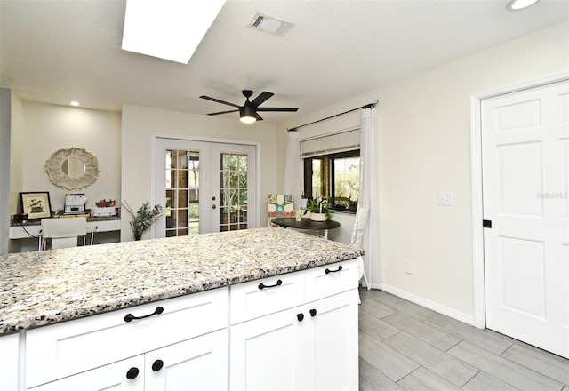 26 Canter Club Ct, Debary, FL 32713 - kitchen with french doors, white cabinets, light stone counters, a skylight, and ceiling fan