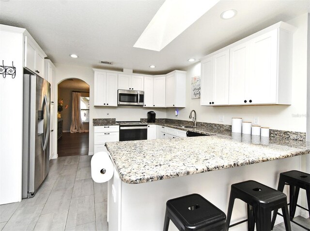 26 Canter Club Ct, Debary, FL 32713 - kitchen featuring appliances with stainless steel finishes, a peninsula, arched walkways, recessed lighting, and a breakfast bar area
