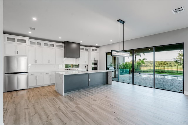 15942 Vetta Dr, Bella Collina, FL 34756 - kitchen with stainless steel appliances, light countertops, ventilation hood, light wood finished floors, and white cabinetry