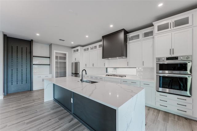 15942 Vetta Dr, Bella Collina, FL 34756 - kitchen with premium range hood, stainless steel appliances, a center island with sink, light wood-style floors, and light stone countertops