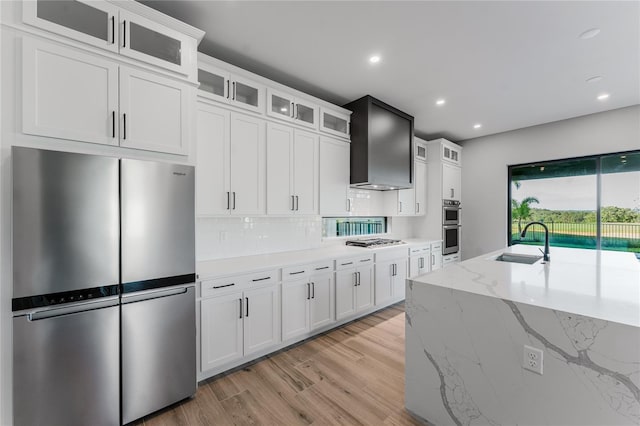 15942 Vetta Dr, Bella Collina, FL 34756 - kitchen with appliances with stainless steel finishes, wall chimney range hood, light wood-type flooring, backsplash, and white cabinetry