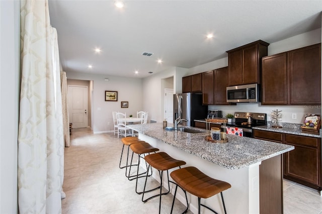 5029 Grand Teton Ct, Deland, FL 32724 - kitchen with appliances with stainless steel finishes, a breakfast bar, an island with sink, dark brown cabinetry, and light stone countertops