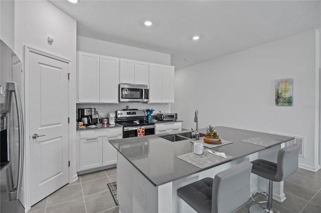 873 Daring Dr, Davenport, FL 33837 - kitchen featuring appliances with stainless steel finishes, a kitchen breakfast bar, light tile patterned floors, a center island with sink, and white cabinets