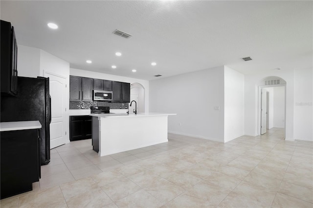 1565 Diamond Loop Dr, Kissimmee, FL 34744 - kitchen featuring stainless steel microwave, arched walkways, decorative backsplash, light countertops, and an island with sink