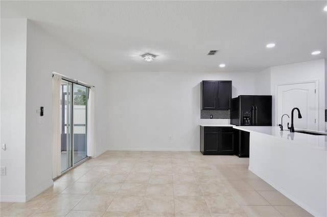 1565 Diamond Loop Dr, Kissimmee, FL 34744 - kitchen with black fridge, light countertops, recessed lighting, dark cabinetry, and decorative backsplash