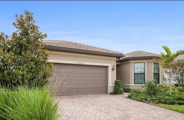 13084 Rinella St, Venice, FL 34293 - view of front of house featuring an attached garage, a tiled roof, decorative driveway, and stucco siding