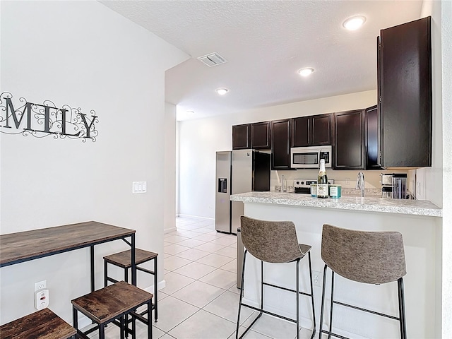 129 Boydfield Ln, Davenport, FL 33837 - kitchen featuring stainless steel appliances, a peninsula, a kitchen bar, light countertops, and light tile patterned flooring