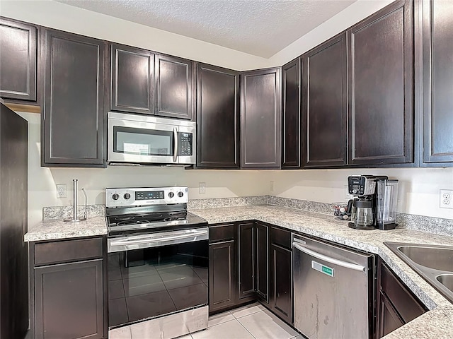129 Boydfield Ln, Davenport, FL 33837 - kitchen with appliances with stainless steel finishes, light countertops, light tile patterned floors, dark brown cabinets, and a textured ceiling