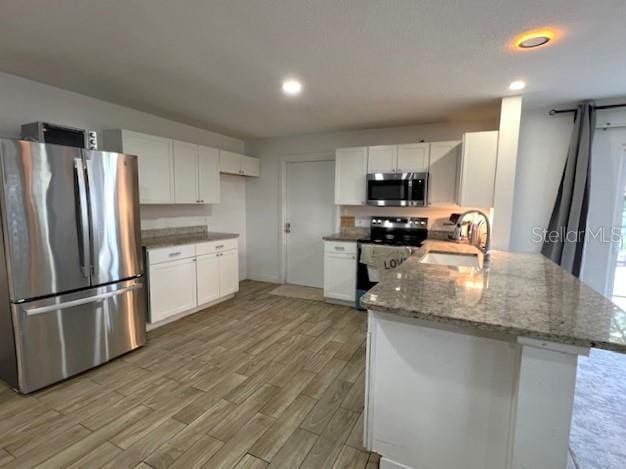 9148 Oakwood Dr, Lake Wales, FL 33898 - kitchen with appliances with stainless steel finishes, a peninsula, light wood-style flooring, white cabinets, and light stone countertops