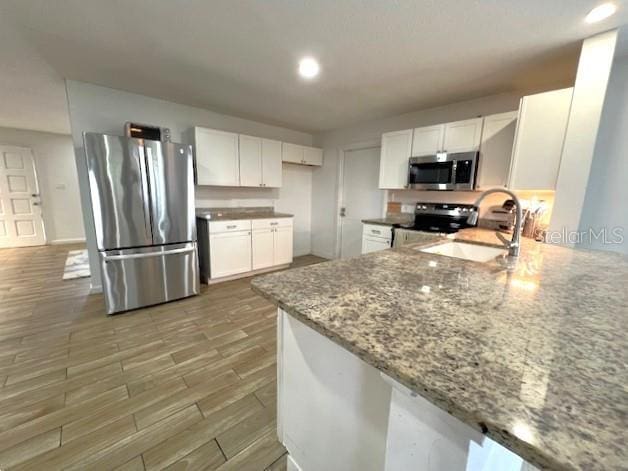 9148 Oakwood Dr, Lake Wales, FL 33898 - kitchen with stainless steel appliances, white cabinets, light stone counters, light wood-style floors, and recessed lighting