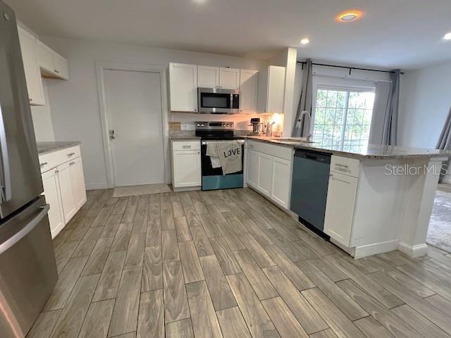 9148 Oakwood Dr, Lake Wales, FL 33898 - kitchen featuring appliances with stainless steel finishes, light wood-style floors, a peninsula, recessed lighting, and white cabinetry
