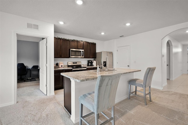 1351 Fox Squirrel Dr, Davenport, FL 33897 - kitchen featuring stainless steel appliances, arched walkways, light colored carpet, a kitchen bar, and dark brown cabinets