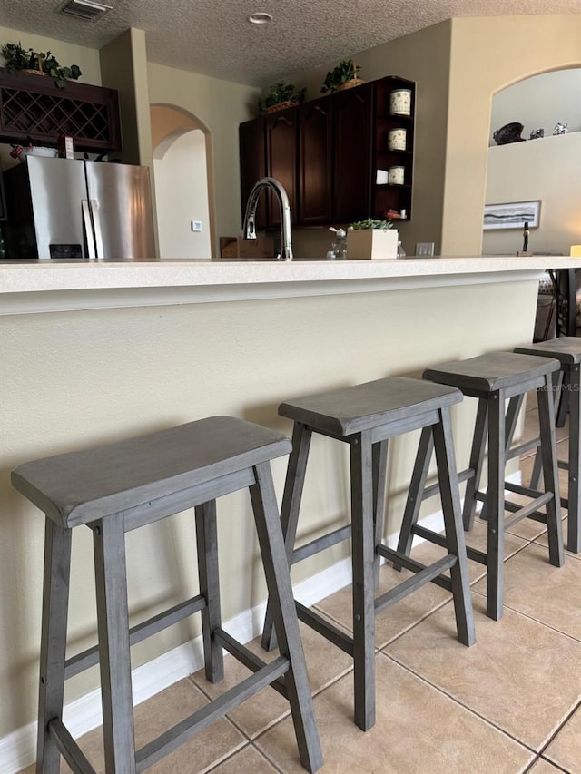 5040 Rock Rose Loop, Sanford, FL 32771 - kitchen featuring stainless steel refrigerator with ice dispenser, arched walkways, a textured ceiling, light countertops, and a breakfast bar
