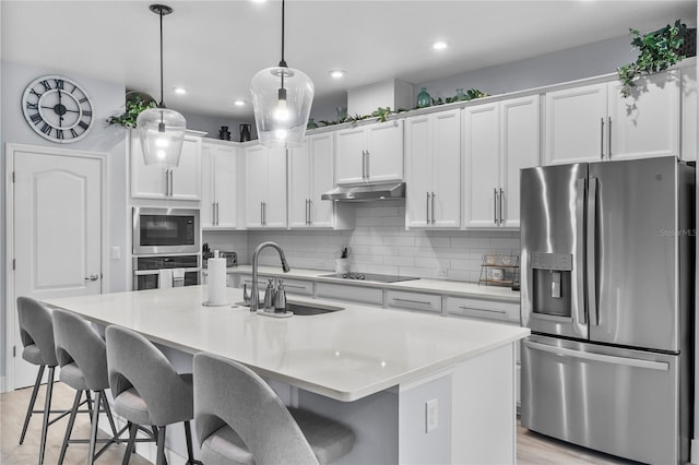 17676 Passionflower Cir, Clermont, FL 34714 - kitchen with appliances with stainless steel finishes, under cabinet range hood, a kitchen breakfast bar, decorative backsplash, and white cabinets
