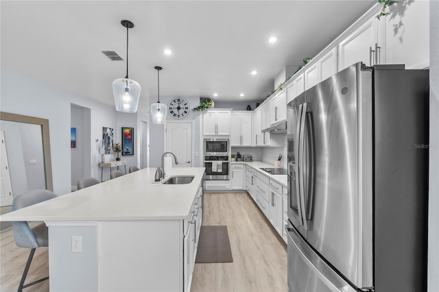 17676 Passionflower Cir, Clermont, FL 34714 - kitchen featuring appliances with stainless steel finishes, under cabinet range hood, a kitchen breakfast bar, light wood-style flooring, and white cabinetry