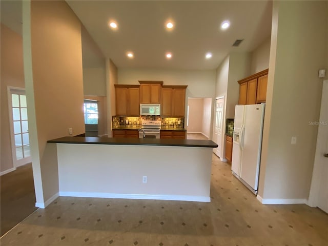 1227 Juniper Hammock St, Winter Garden, FL 34787 - kitchen with white appliances, dark countertops, a peninsula, decorative backsplash, and brown cabinets
