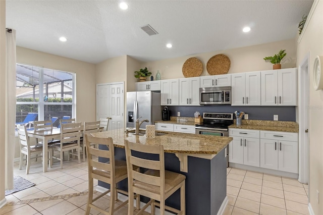 2222 Wyndham Palms Way, Kissimmee, FL 34747 - kitchen with appliances with stainless steel finishes, light tile patterned flooring, a kitchen island with sink, a kitchen bar, and light stone countertops