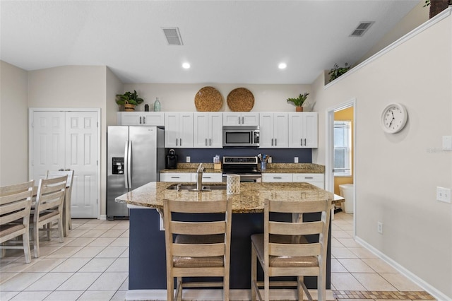 2222 Wyndham Palms Way, Kissimmee, FL 34747 - kitchen with stainless steel appliances, light tile patterned floors, an island with sink, white cabinets, and a kitchen breakfast bar