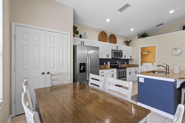 2222 Wyndham Palms Way, Kissimmee, FL 34747 - kitchen with stainless steel appliances, washer and dryer, lofted ceiling, light tile patterned floors, and white cabinets