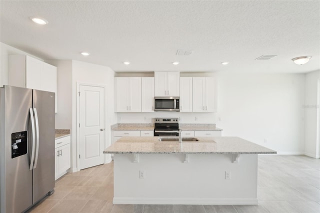 1349 Oak Valley Dr, Auburndale, FL 33823 - kitchen with stainless steel appliances, an island with sink, light stone countertops, white cabinets, and a textured ceiling