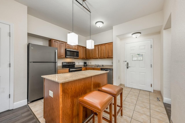12527 Floridays Resort Dr Unit E104, Orlando, FL 32821 - kitchen featuring stainless steel appliances, a center island, brown cabinetry, pendant lighting, and light stone counters