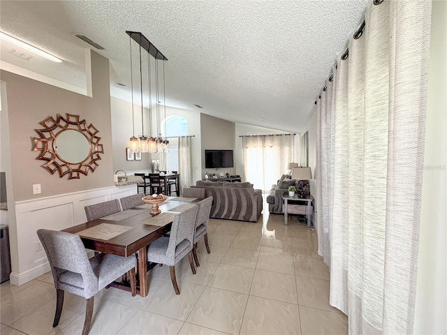 150 Barefoot Beach Way, Kissimmee, FL 34746 - dining room featuring lofted ceiling, a textured ceiling, light tile patterned floors, and a wainscoted wall