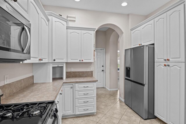 5339 Pond Crossing Pl, Leesburg, FL 34748 - kitchen featuring appliances with stainless steel finishes, arched walkways, light countertops, white cabinetry, and light tile patterned flooring