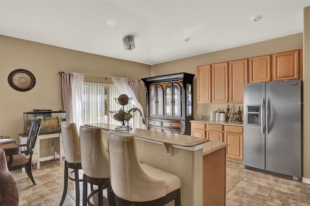 501 Lake Cummings Way, Lake Alfred, FL 33850 - kitchen with stainless steel fridge with ice dispenser, a breakfast bar area, light countertops, light tile patterned floors, and light brown cabinetry