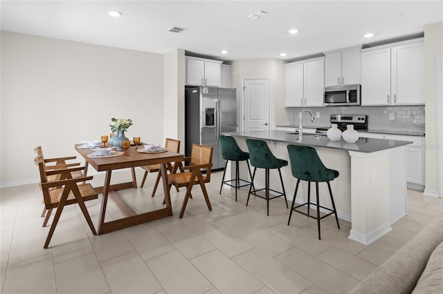 2817 Muller Oak Loop, Ocoee, FL 34761 - kitchen with appliances with stainless steel finishes, a kitchen bar, decorative backsplash, a kitchen island with sink, and white cabinets