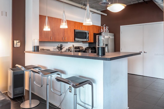 10 N Summerlin Ave Unit 14, Orlando, FL 32801 - kitchen featuring appliances with stainless steel finishes, brown cabinets, dark countertops, a kitchen bar, and dark tile patterned flooring