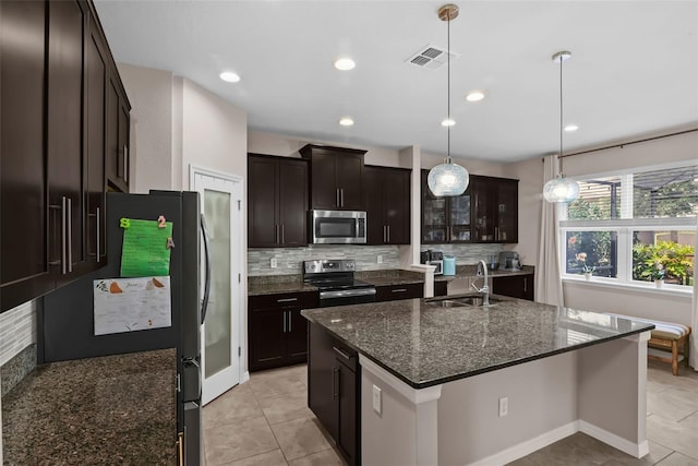 3472 Gretchen Dr, Ocoee, FL 34761 - kitchen with appliances with stainless steel finishes, a center island with sink, backsplash, dark stone counters, and decorative light fixtures