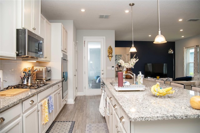 5963 Glory Bower Dr, Winter Garden, FL 34787 - kitchen with stainless steel appliances, a spacious island, white cabinets, tasteful backsplash, and light wood-style floors