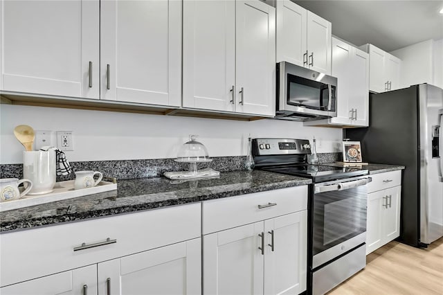 9937 Aqua Miles Path, Wesley Chapel, FL 33545 - kitchen with stainless steel appliances, light wood finished floors, white cabinets, and dark stone countertops