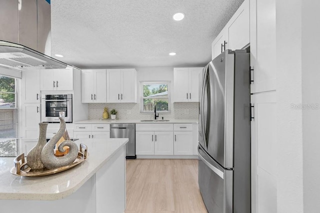 3029 Pinetree, Winter Haven, FL 33884 - kitchen featuring appliances with stainless steel finishes, island exhaust hood, a textured ceiling, white cabinets, and light wood finished floors