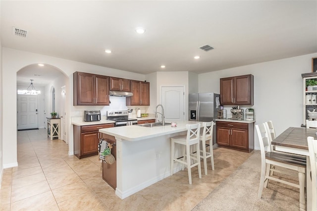 1010 Morvan Ln, Kissimmee, FL 34759 - kitchen featuring appliances with stainless steel finishes, under cabinet range hood, arched walkways, light countertops, and a center island with sink
