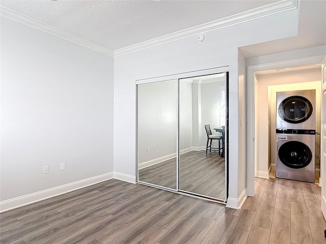 60 Surfview Dr Unit 308, Palm Coast, FL 32137 - unfurnished bedroom featuring stacked washing machine and dryer, wood finished floors, a closet, crown molding, and a textured ceiling