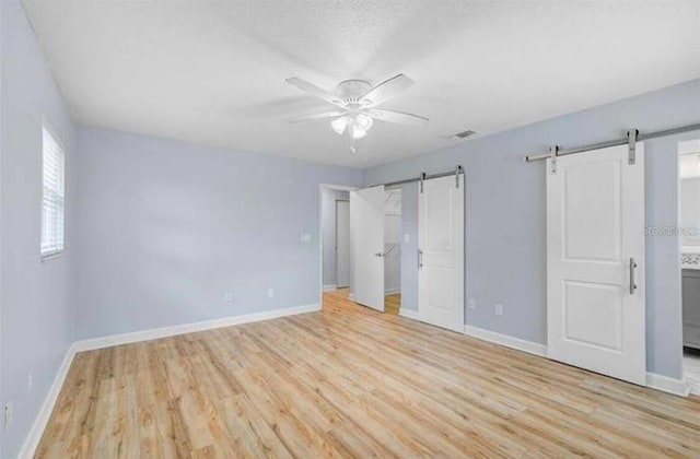2813 21st Ave W, Bradenton, FL 34205 - unfurnished bedroom with a barn door, wood finished floors, ensuite bath, and ceiling fan