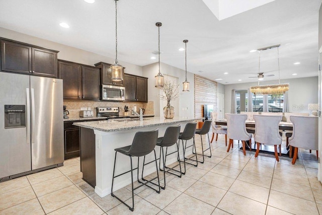8901 Rhodes St, Kissimmee, FL 34747 - kitchen featuring appliances with stainless steel finishes, backsplash, a kitchen bar, dark brown cabinets, and light tile patterned floors