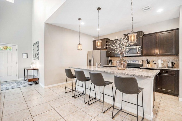 8901 Rhodes St, Kissimmee, FL 34747 - kitchen featuring stainless steel appliances, a kitchen bar, tasteful backsplash, an island with sink, and dark brown cabinetry
